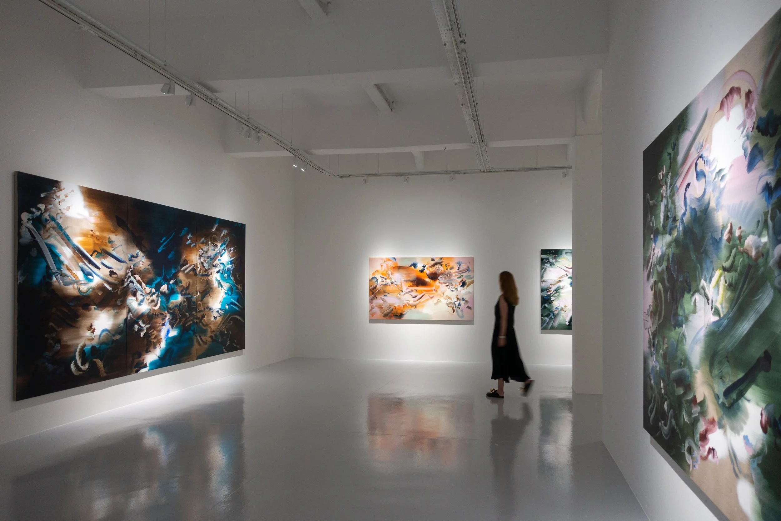 A contemporary art gallery with large abstract works and a person walking through the space.